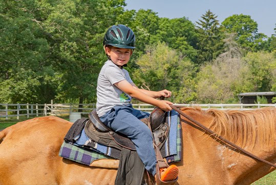 young child riding on horse during camp